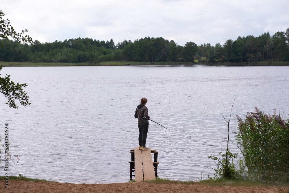 Fisherman with rod, spinning reel on the river bank. Fishing for pike, perch, carp. catching fish, pulling rod while fishing at the weekend. Girl fishing from beach lake or pond with text space. Fisherman with rod, spinning reel on the river bank. Fishing for pike, perch, carp. catching fish, pulling rod while fishing at the weekend. Girl fishing from beach lake or pond with text space.