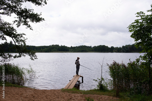 Fisherman with rod, spinning reel on the river bank. Fishing for pike, perch, carp. catching fish, pulling rod while fishing at the weekend. Girl fishing from beach lake or pond with text space.