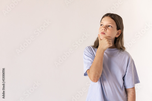 Portrait of pensive preteen girl looking away. Caucasian child wearing blue T-shirt thinking rubbing her chin against white background. Dreaming concept