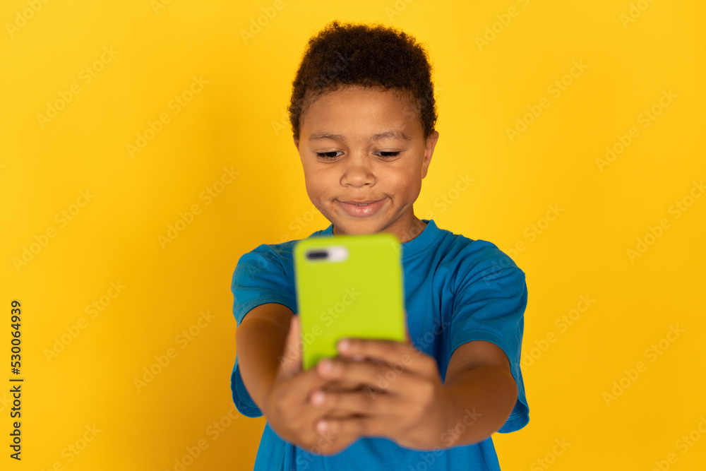 Portrait of concentrated preteen boy using smartphone. Mixed race child wearing blue T-shirt surfing internet or watching video on cellphone. Social networking and technology concept Portrait of concentrated preteen boy using smartphone. Mixed race child wearing blue T-shirt surfing internet or watching video on cellphone. Social networking and technology concept