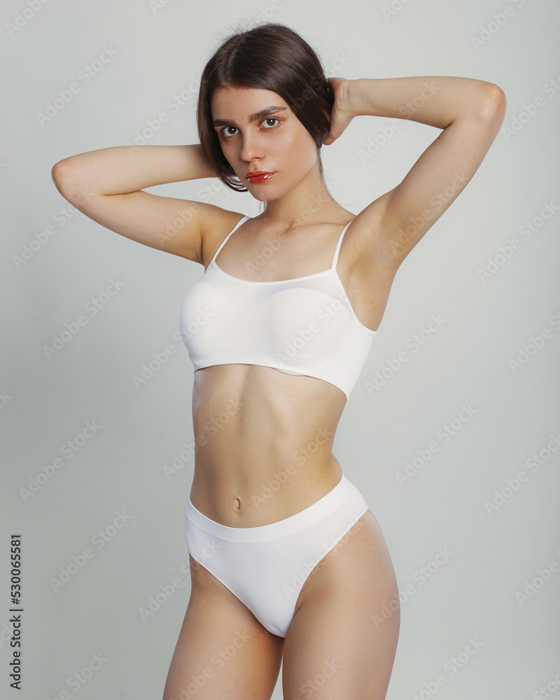 Young woman posing in a in white casual underwear on gray background in studio, copy space. Seductive woman perfect body. Sexy fashion model wear underwear.
