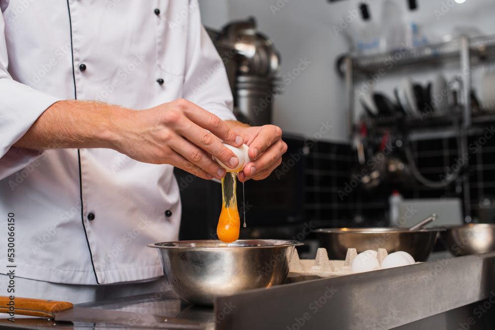 cropped view of man breaking raw egg above bowl while cooking in kitchen. cropped view of man breaking raw egg above bowl while cooking in kitchen.