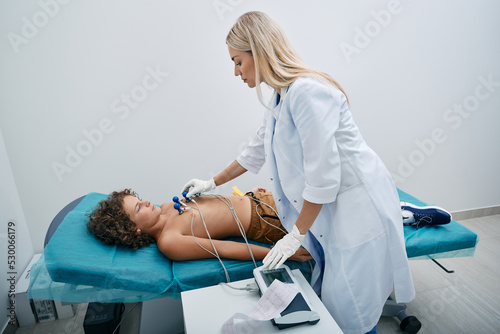 Cardiologist installing vacuum sensors on male child chest during electrocardiogram procedure at medical clinic. ECG for children photo