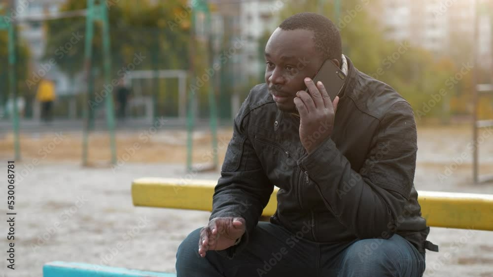 African american man sits at sport ground and talks on smartphone, real talks African american man sits at sport ground and talks on smartphone, real talks