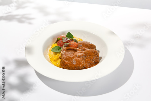 Traditional italian dish - osso buco with risotto milanese. Stew meat on bone with rice on white plate. Summer italian dining. Italian osso buco with garnish with hard shadows