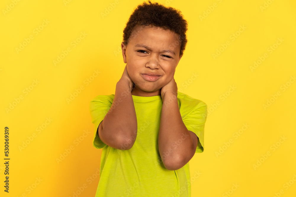 Portrait of displeased preteen boy rubbing neck. Mixed race child wearing green T-shirt suffering from neck ache. Childs health problems concept Portrait of displeased preteen boy rubbing neck. Mixed race child wearing green T-shirt suffering from neck ache. Childs health problems concept