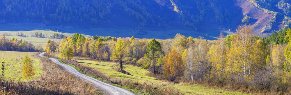 Autumn road, scenic panoramic view. Yellow trees on a background of blue mountainside.
