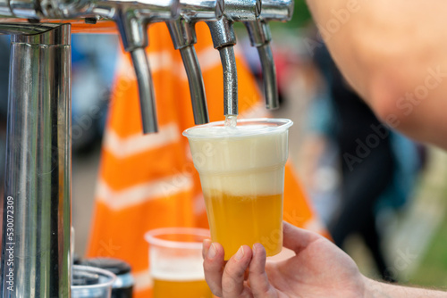 Bartender's hands in the process of pouring beer into a plastic glass