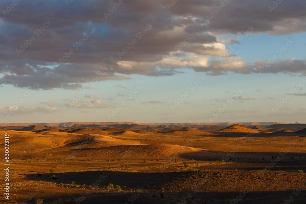 Sunset in the Sahara desert. Top view of the valley. Rocky hills and cloudy sky.