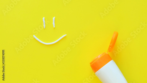 Smiling face from sunscreen and cosmetic tube on a solid yellow background. Protect skin from sun