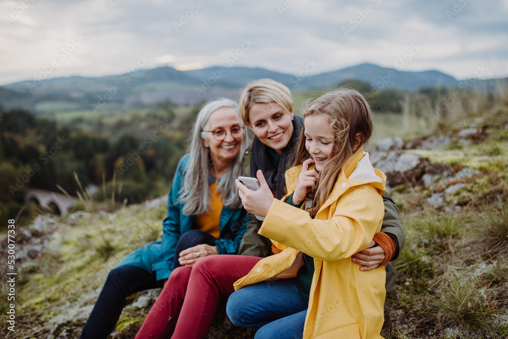 Small girl with mother and grandmother checking smartphone outoors on top of mountain. Small girl with mother and grandmother checking smartphone outoors on top of mountain.