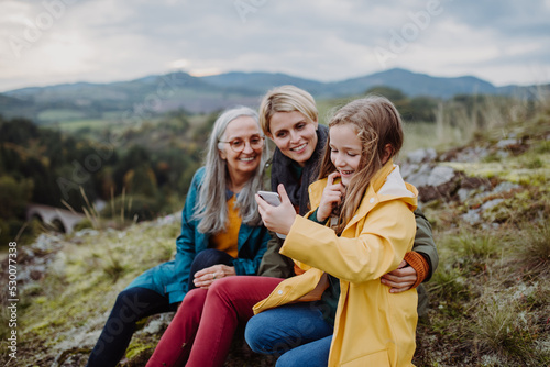 Small girl with mother and grandmother checking smartphone outoors on top of mountain.