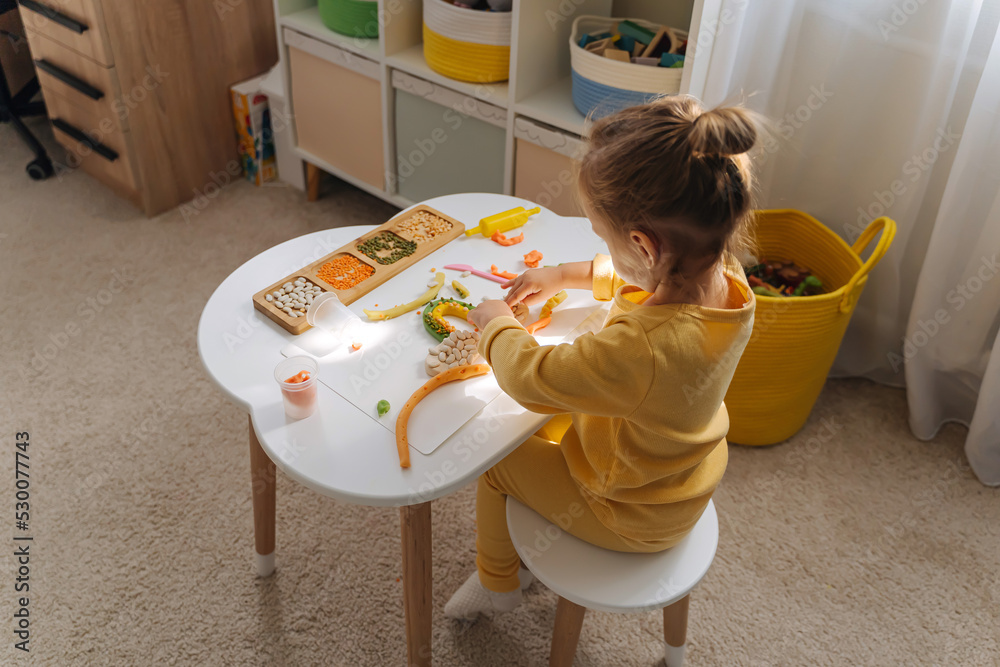 A little girl playing with rainbow from play dough for modeling with decorate from dried beans