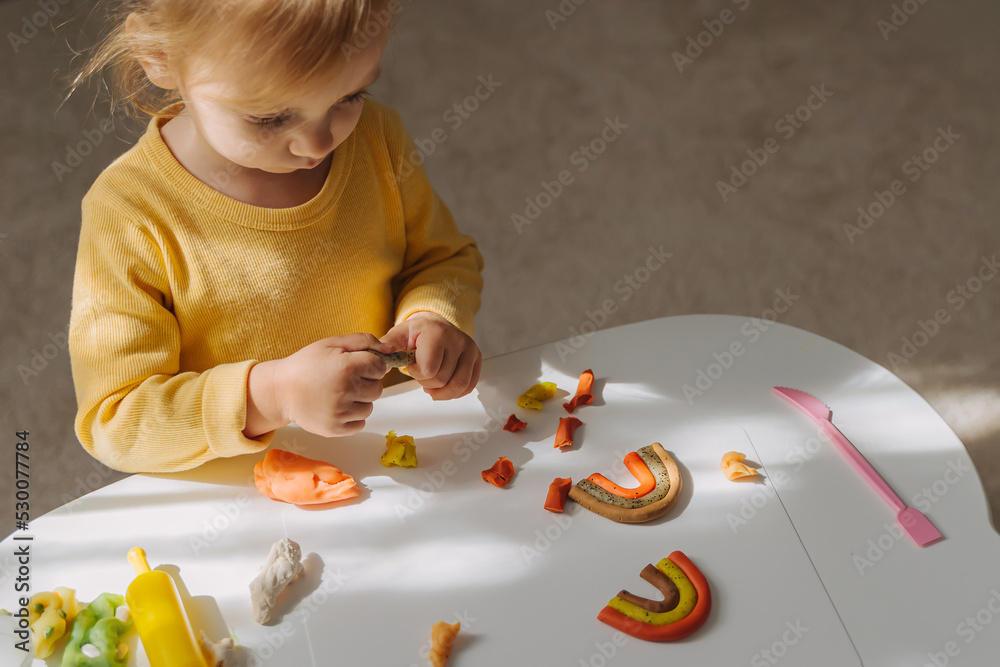 A little girl playing with rainbow from play dough for modeling. Art Activity for Kids. Fine