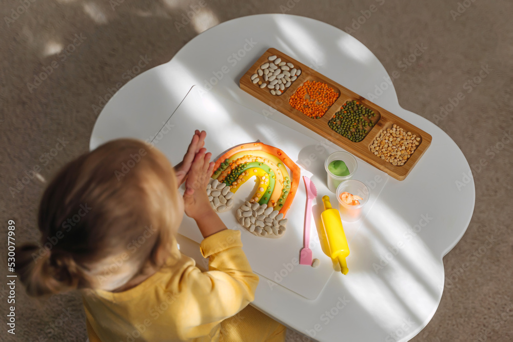 A little girl playing with rainbow from play dough for modeling with decorate from dried beans