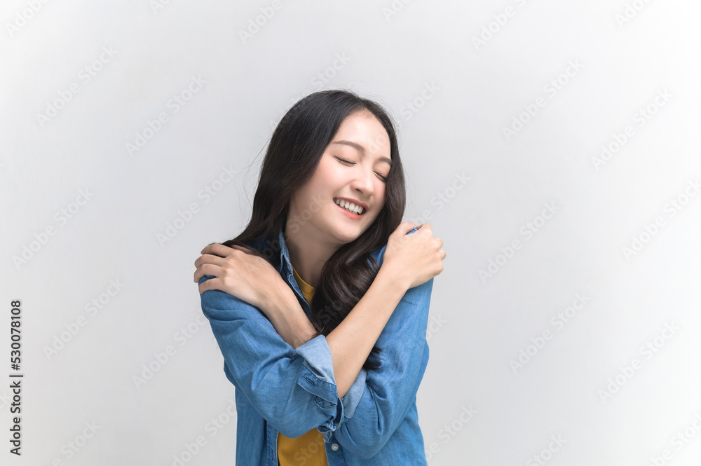 Self care and self esteem concept, Happy young beautiful Asian woman in colorful clothing hugging herself isolated on white background. People emotion portrait concept. Self care and self esteem concept, Happy young beautiful Asian woman in colorful clothing hugging herself isolated on white background. People emotion portrait concept.