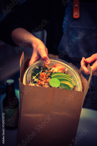 Photo of a woman putting poke bowl in a bag
