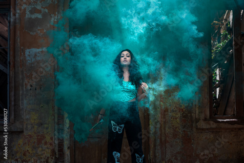 Young girl posing with turquoise smoke in an abandoned place