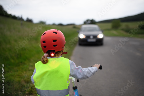 Rear view of child riding bike on road with car in front of her, road safety education concept.