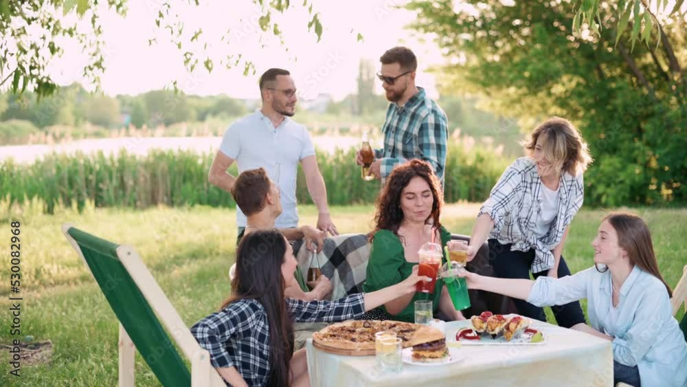 Group of friends are relaxing together outdoor. Young cheerful people clink glasses and laugh.