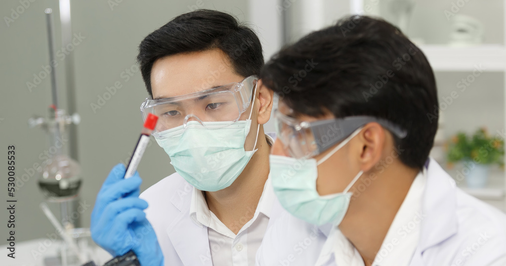 Two Male Scientists with Mask working in Lab while Checking Result of Blood Sample testing. Two Male Scientists with Mask working in Lab while Checking Result of Blood Sample testing.