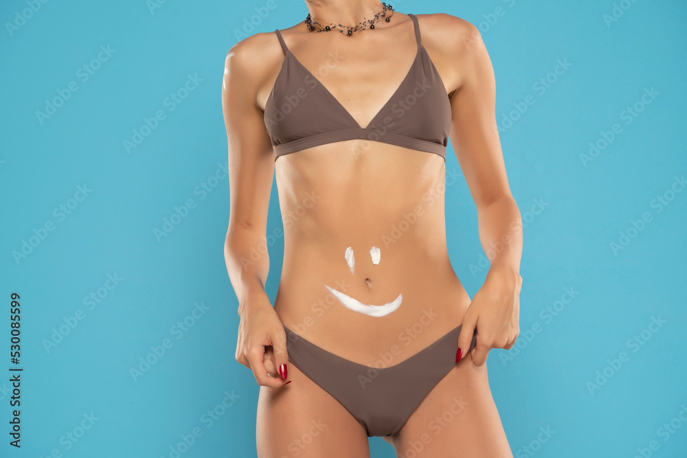 Fototapeta premium Woman's belly close-up with smile drawn with lotion on a blue background