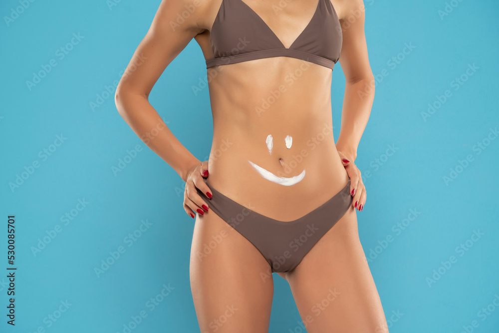 Woman's belly close-up with smile drawn with lotion on a blue background