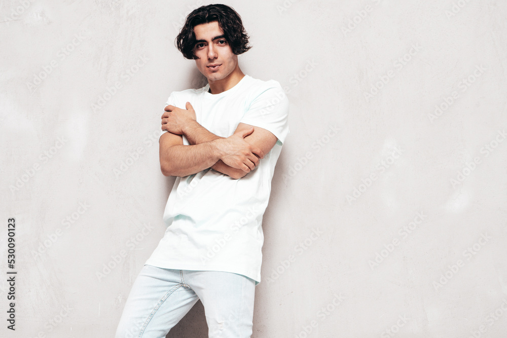 Portrait of handsome confident  stylish hipster lambersexual model.Sexy man dressed in over size T-shirt and jeans. Fashion male isolated in studio. Posing near grey wall