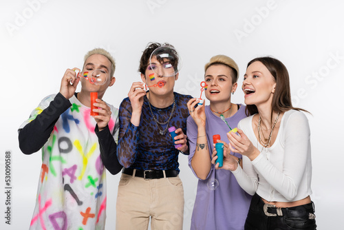 joyful lgbtq community friends having fun and blowing soap bubbles isolated on grey.
