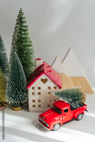 Miniature house and fir trees with red car with Christmas Tree on white background. Winter cute landscape. Cozy small world. Christmas decorations, holiday concept.