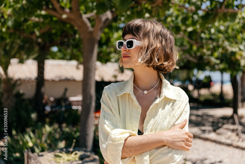 Obraz na płótnie Adorable stylish lovely girl with short wavy hairstyle wearing bright sunglasses and linen suit posing in sunlight w salonie