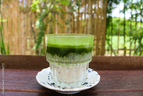 Matcha latte green tea with milk in glass on wooden table.