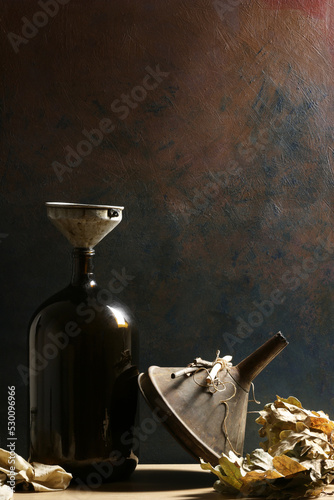 Composizione verticale con bottiglia, imbuti, foglie di quercia; still life su fondo scuro photo