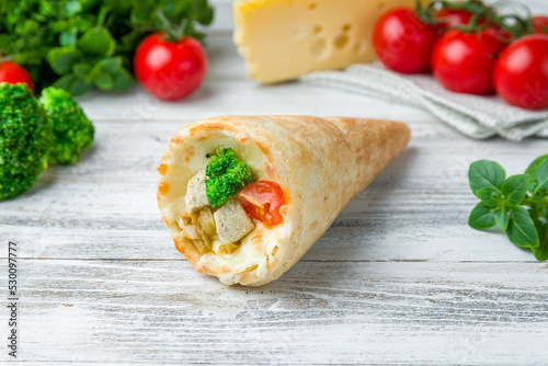 pizza in a cone with chicken, tomato and broccoli on white wooden table