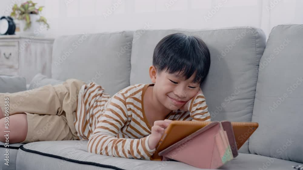 4K, slow motion, Handsome Asian boy, lying on sofa in his comfortable position, along with hands on feet, chin, Boy laying down watching online clips on his tablet merrily, his face looked happy. 4K, slow motion, Handsome Asian boy, lying on sofa in his comfortable position, along with hands on feet, chin, Boy laying down watching online clips on his tablet merrily, his face looked happy.