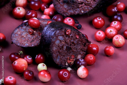 Baked blood sausage on a red plate decorated with red cranberries, Traditional Latvian blood sausages photo