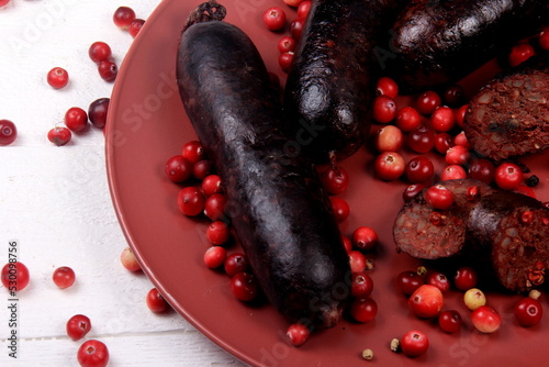 Baked blood sausage on a red plate decorated with red cranberries, Traditional Latvian blood sausages photo