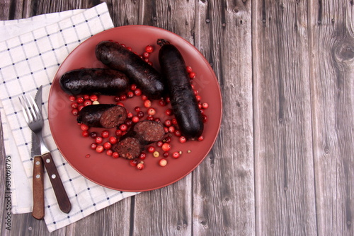 Baked blood sausage on a red plate decorated with red cranberries, Traditional Latvian blood sausages photo