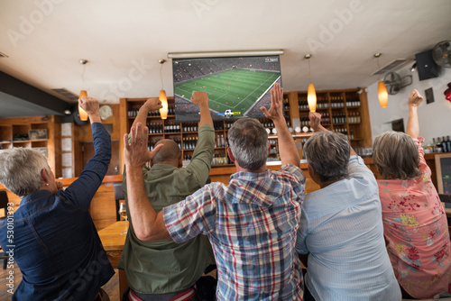 Group of senior diverse friends sitting in the bar and watching football match