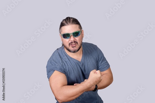 A stocky and burly man wearing shades raises his sleeve to expose his arms, flexing his biceps. Grunting while trying to look big. photo