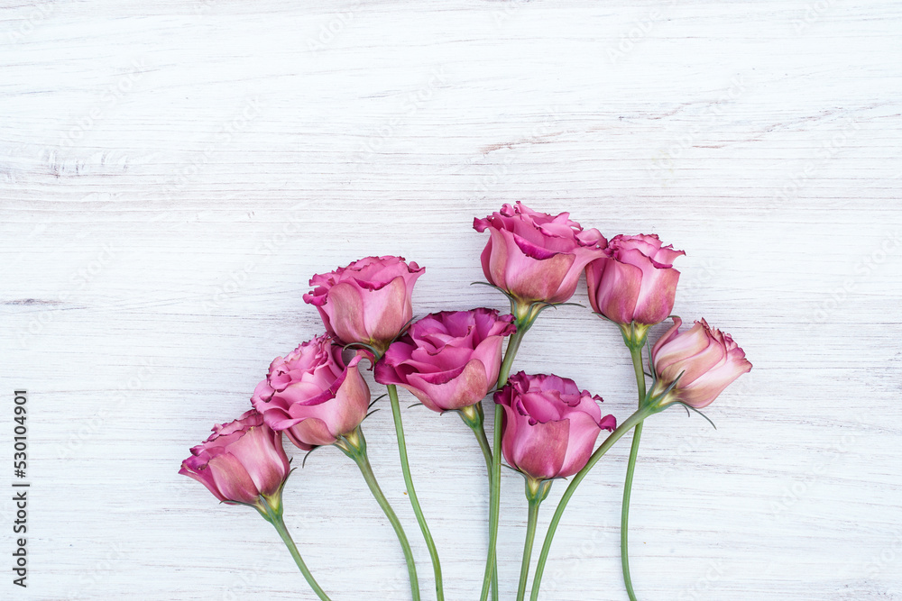 A bouquet of eight light pink lisianthus flowers on a wood background. Space for text.
