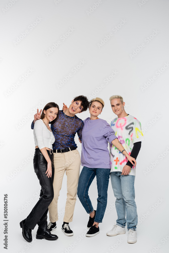 happy queer person showing victory sign near diverse lgbtq friends on grey background. happy queer person showing victory sign near diverse lgbtq friends on grey background.