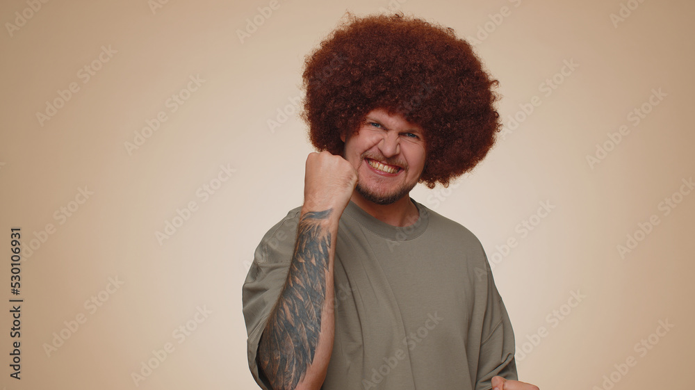 Happy joyful man in casual t-shirt shouting, raising fists in gesture I did it, celebrating success, winning, birthday, lottery goal achievemen. Adult guy boy indoors on beige studio wall background Happy joyful man in casual t-shirt shouting, raising fists in gesture I did it, celebrating success, winning, birthday, lottery goal achievemen. Adult guy boy indoors on beige studio wall background
