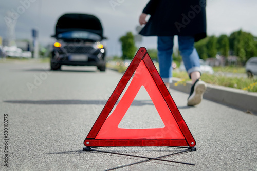 Red warning triangle and a woman walking towards her broken car on the road