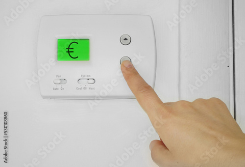Person adjusting a wall thermostat with Euro symbol on the display