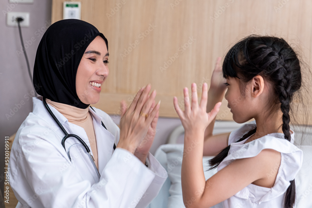A pediatrician in her uniform with stethoscope around neck is having fun with her little girl patient at hospital meeting.Medical insurance background, medical worker, and medicine treatment concepts.