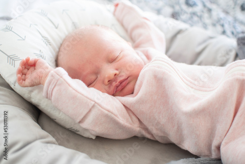 Cute caucasian baby stretching in her sleep. Sleeping newborn baby in a pink bodysuit