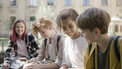 Happy multiethnic school friends talking and laughing during break, having fun