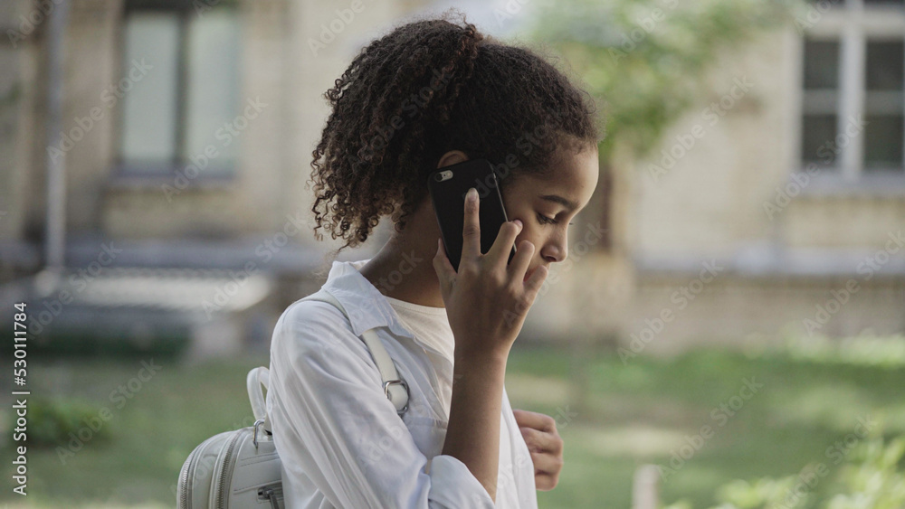 Scared biracial teen girl talking on phone, standing alone in street, calling for help