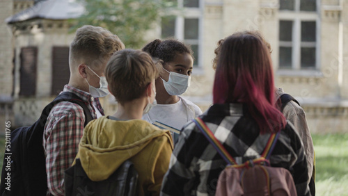 Multiethnic school kids in protective face masks talking after classes, pandemic